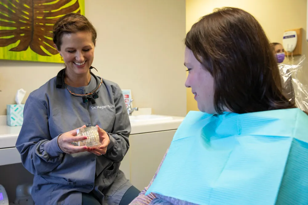 A provider in scrubs explaining treatment options using a hand-held dental model with a seated patient.