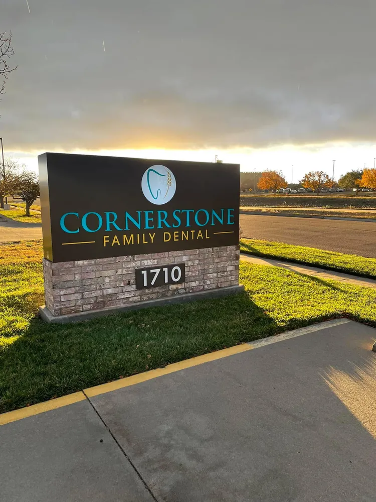Cornerstone Family Dental monument sign at sunset, with the practice&rsquo;s tooth and wheat stalk logo in gold and blue.